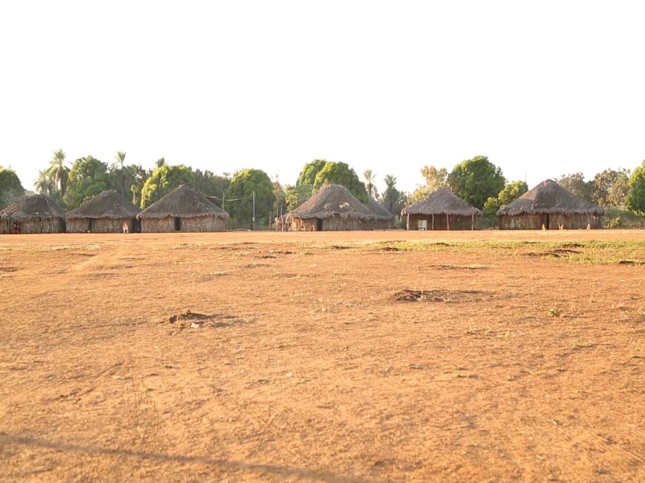 Imagem de aldeia em território indígena mostra construções tradicionais de palha e madeira na linha do horizonte