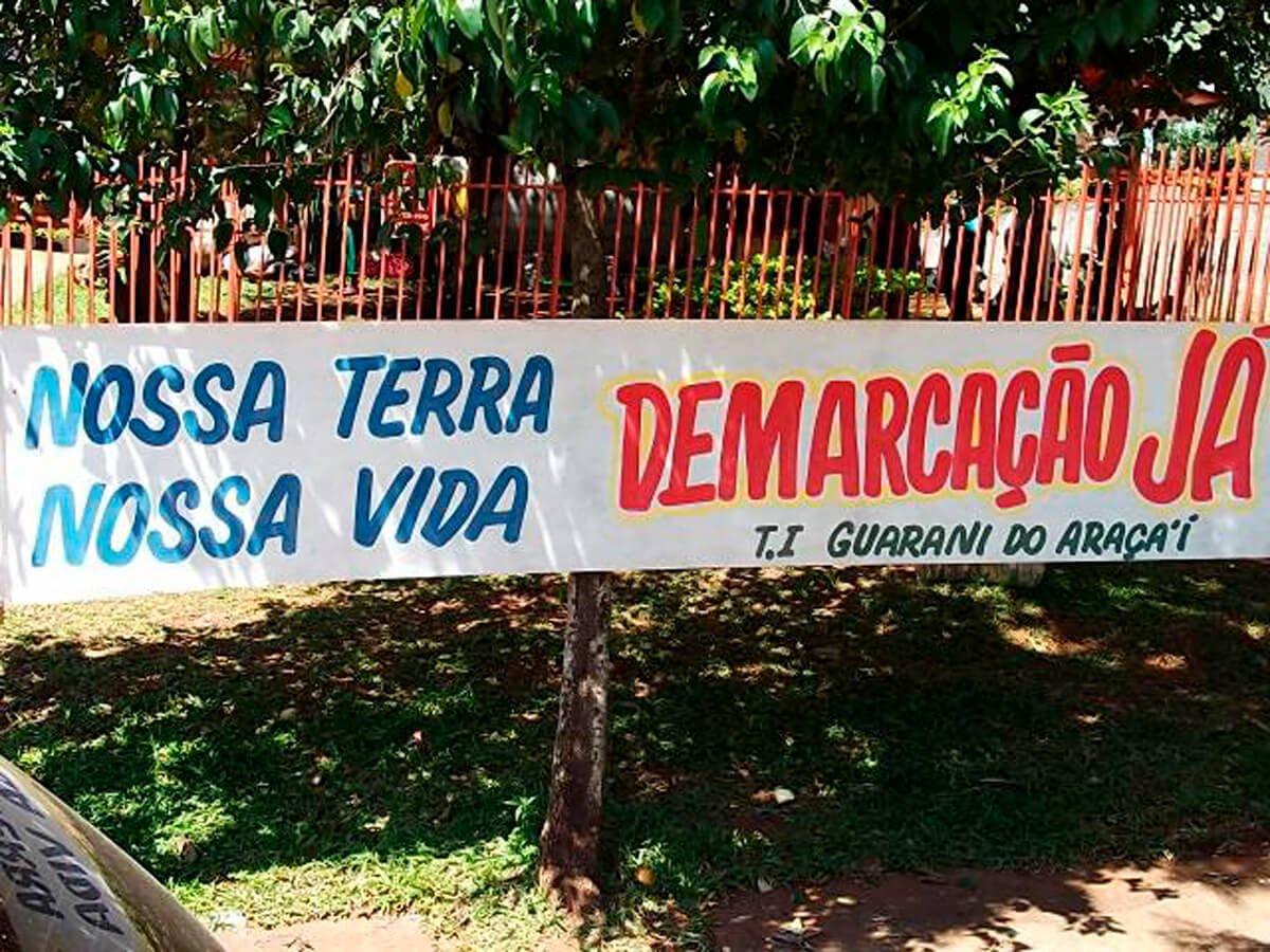 Imagem mostra faixa exposta pelos indígenas Guarani de Araça'í pedindo a demarcação de sua terra, hoje afetada pela tese do marco temporal